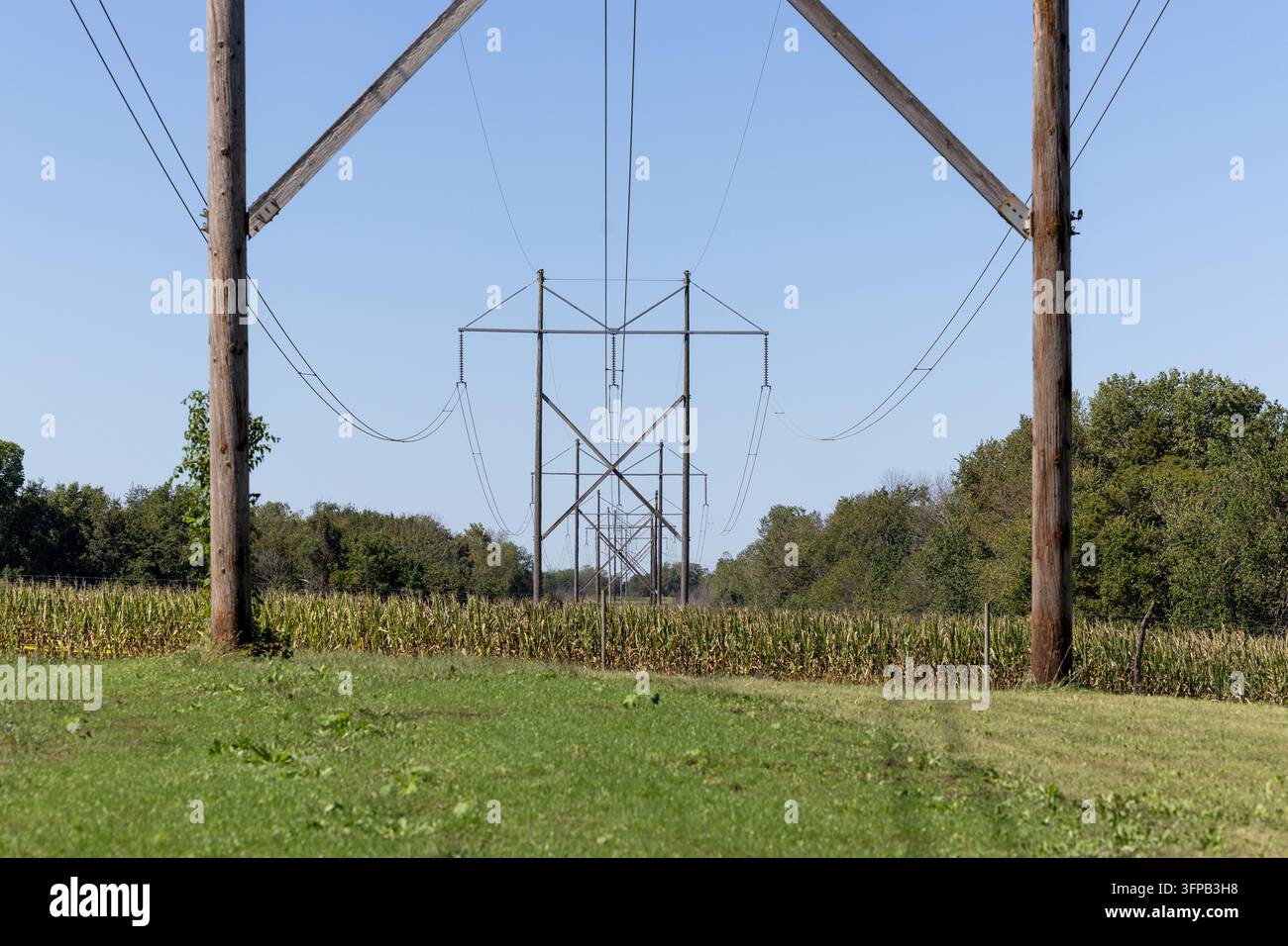 Les poteaux utilitaires en bois et les entretoises en premier plan encadrent les lignes de transmission d'électricité qui s'étendent sur les terres agricoles du Kansas oriental. Banque D'Images