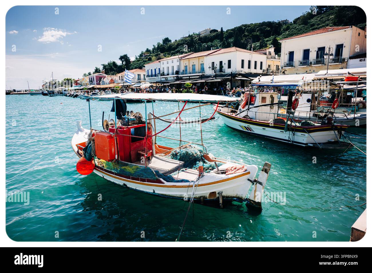 Bateaux de pêche traditionnels grecs amarrés dans les eaux turquoise du port de Katakolo, avec des cafés et des bâtiments en bord de mer en arrière-plan, Péloponnèse Banque D'Images