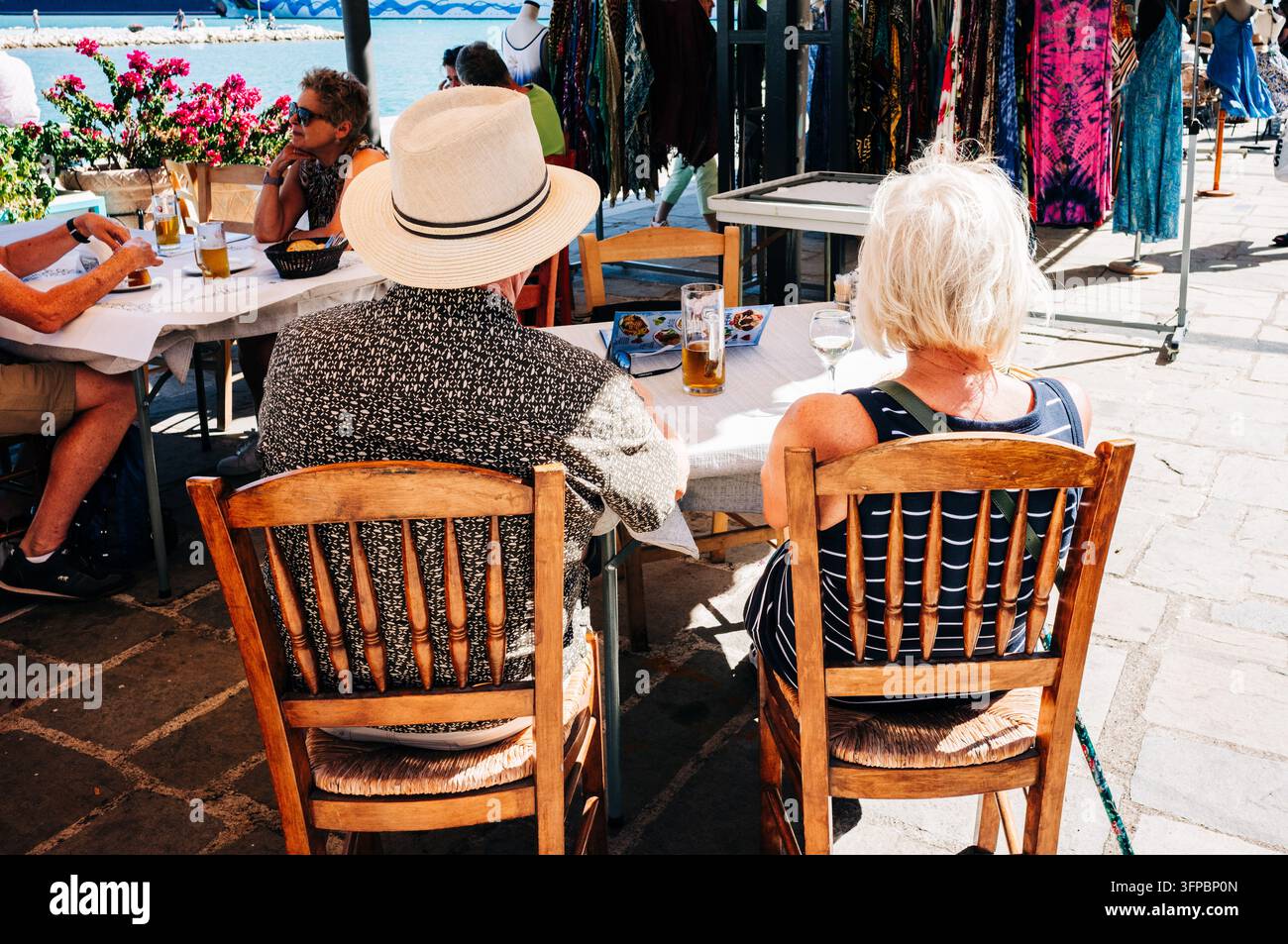Touristes se relaxant dans un café en bord d'eau à côté d'étals de marché colorés à Katakolo, en Grèce occidentale. Banque D'Images