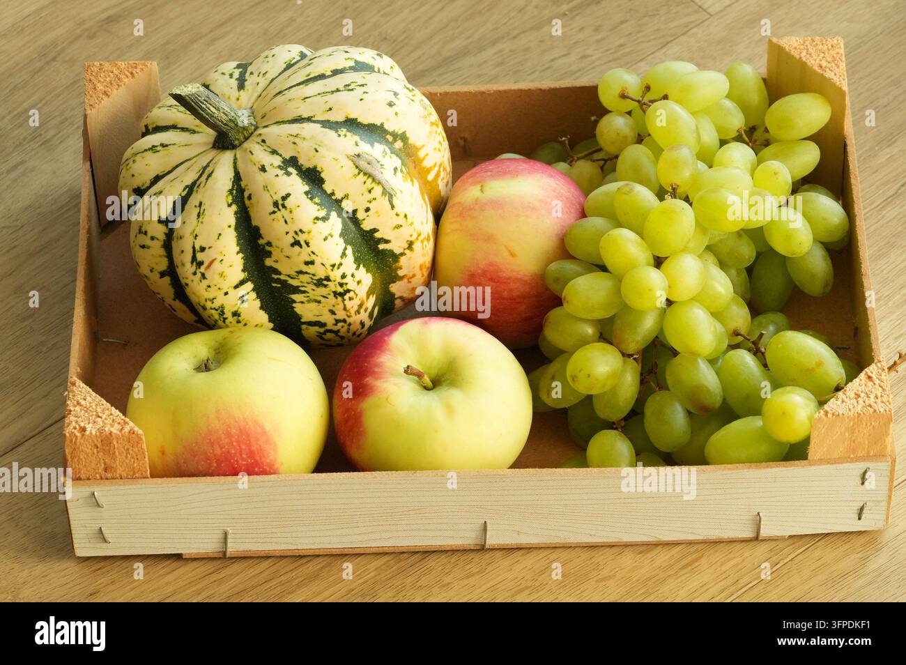 Citrouille, pommes et raisins dans une boîte en bois sur un fond en bois Banque D'Images