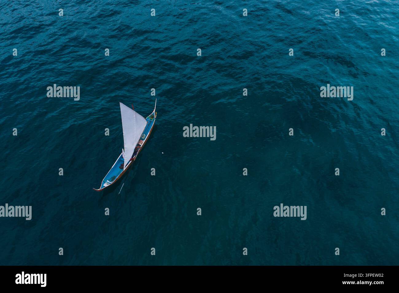Vue aérienne d'un voilier traditionnel avec une voile blanche glissant sur l'océan bleu profond en Indonésie Banque D'Images