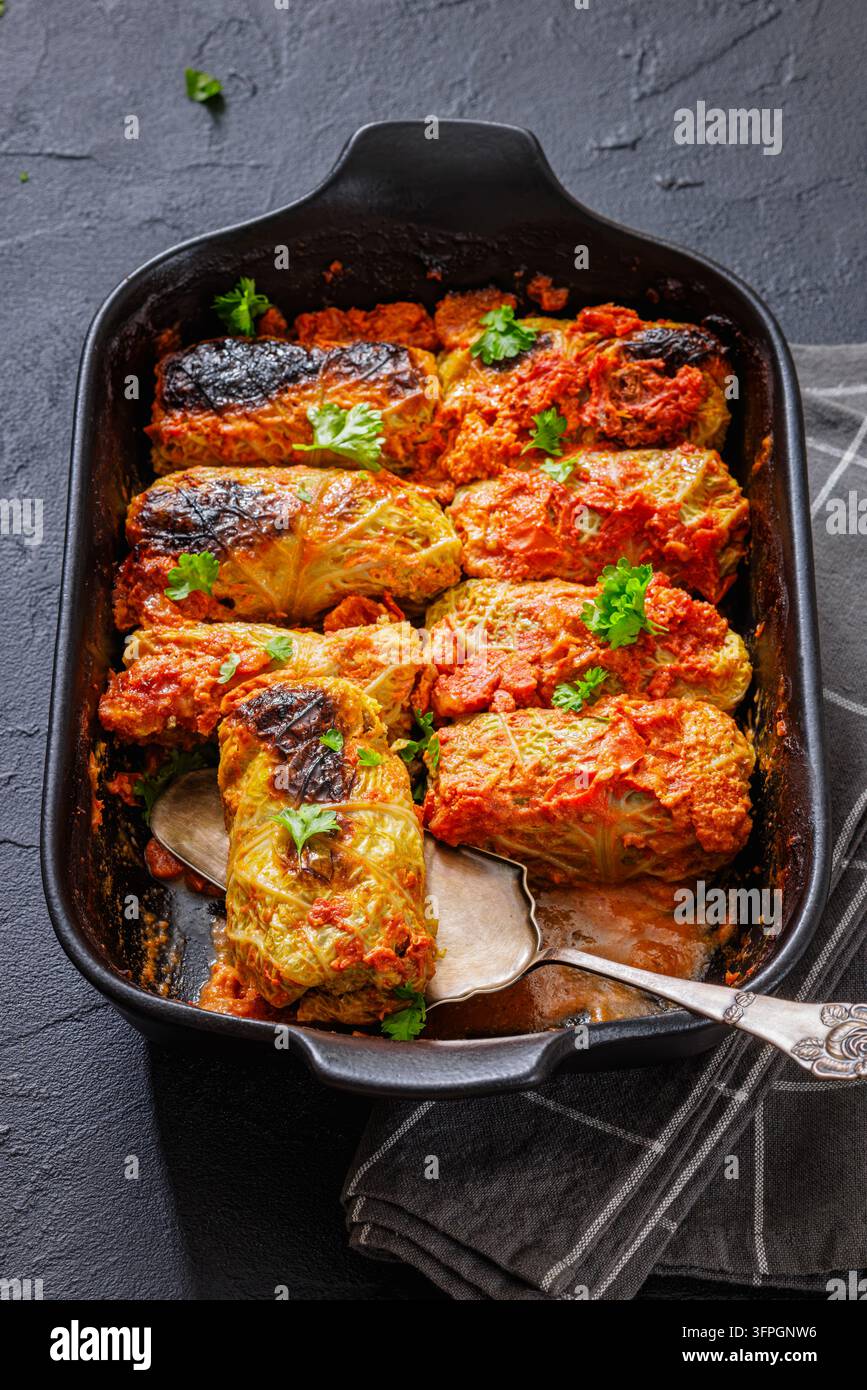 Roulés de chou au chou (Golabki) cuits au four avec une sauce tomate savoureuse, servis avec de la persil frais et une trempette à la crème fraîche dans un plat en céramique noire sur un fond en pierre sombre, Pologne Banque D'Images