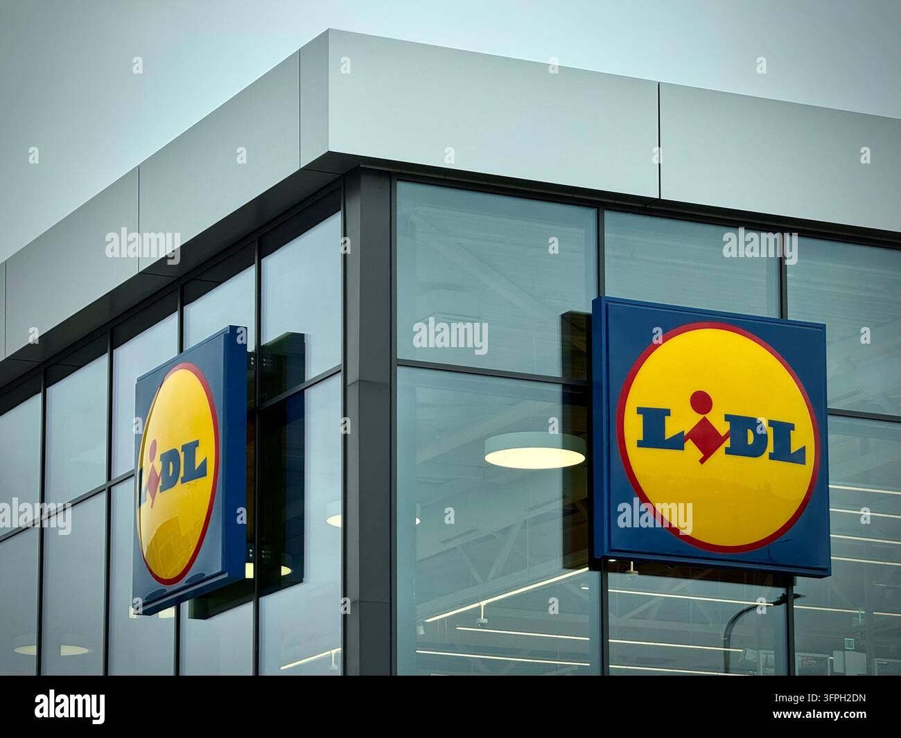 un supermarché Lidl moderne avec des panneaux carrés bleus et jaunes portant le logo, fixés sur un mur-rideau en verre - Image de stock capturée avec un smartphone