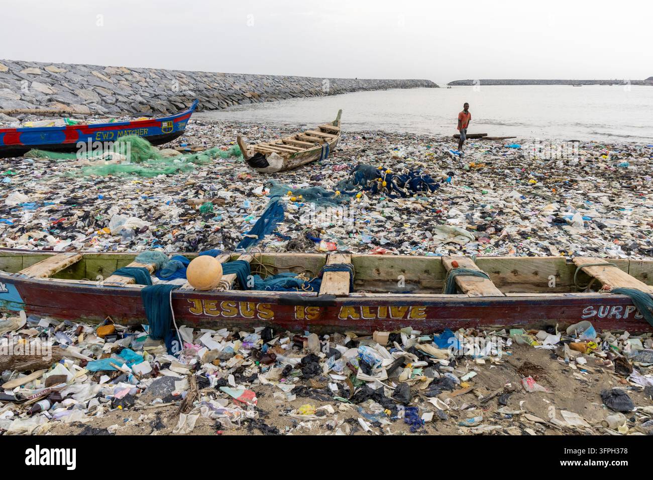 Bateaux de pêche traditionnels en bois peints avec des messages religieux reposant sur une plage couverte de déchets plastiques, Région centrale, Cape Coast, Ghana Banque D'Images