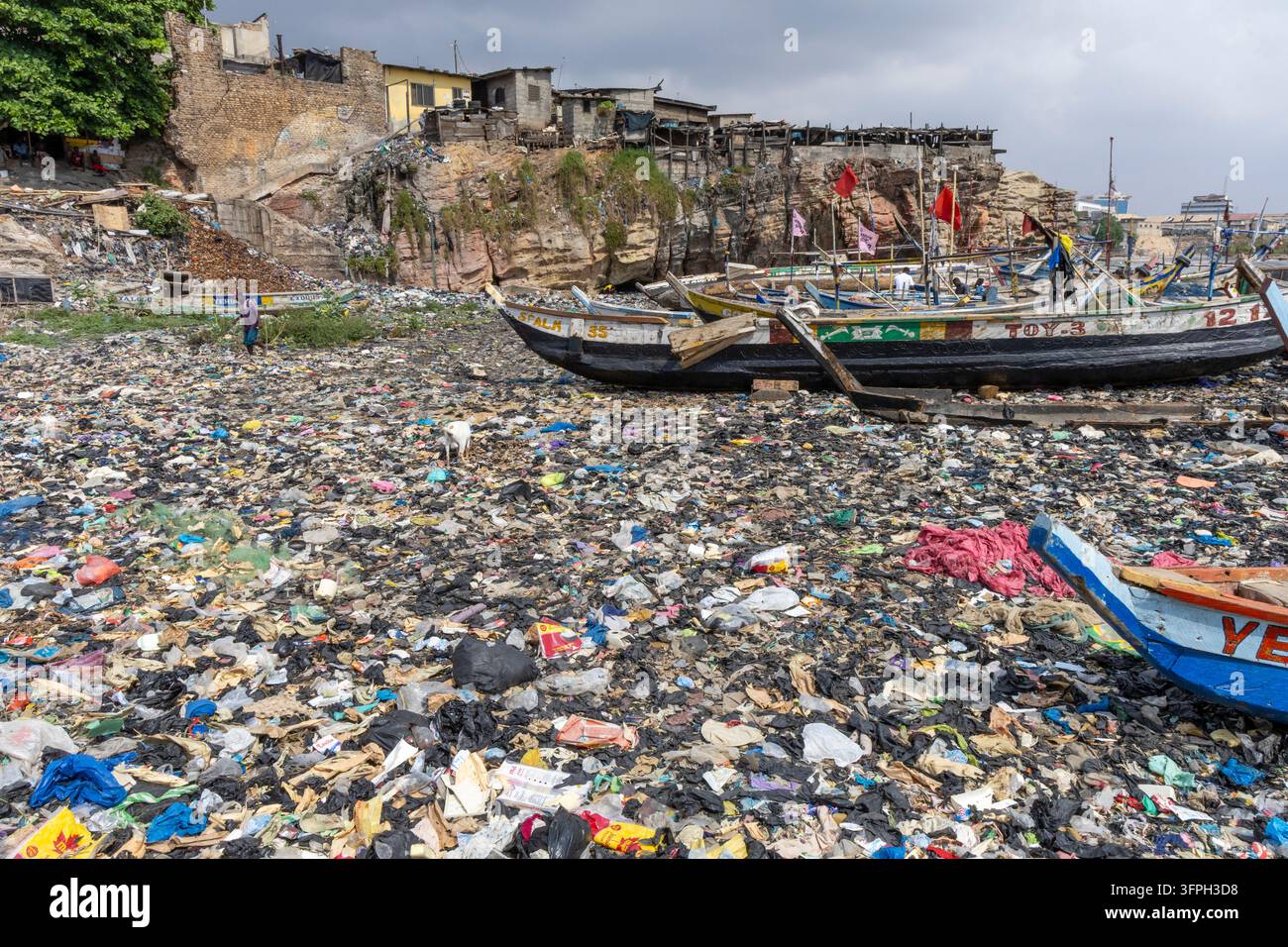 Des bateaux de pêche traditionnels en bois reposent sur une plage ensevelie sous des déchets plastiques en contrebas d'une colonie située sur les falaises, Région de Greater Accra, Accra, Ghana Banque D'Images