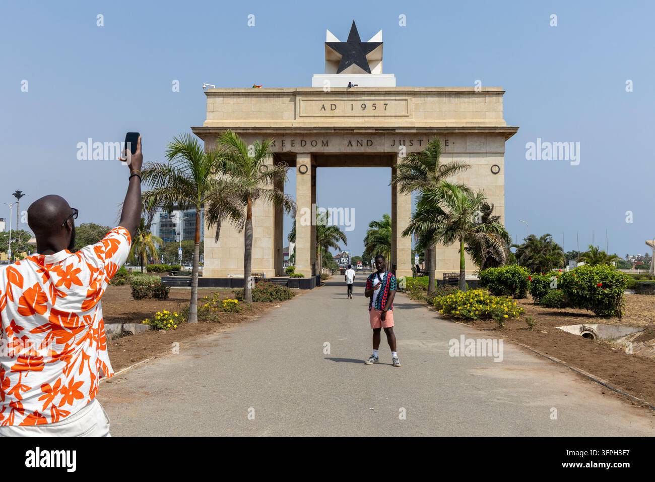 Un homme lève son téléphone pour photographier un compagnon posant devant le monument Black Star Gate, dans la région de Greater Accra, Accra, Ghana Banque D'Images