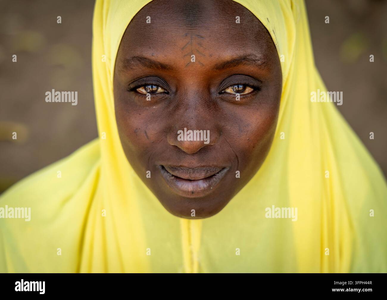Portrait rapproché d'une femme souriante portant un hijab jaune avec des marques faciales, Région de Bono Est, Kintampo, Ghana Banque D'Images
