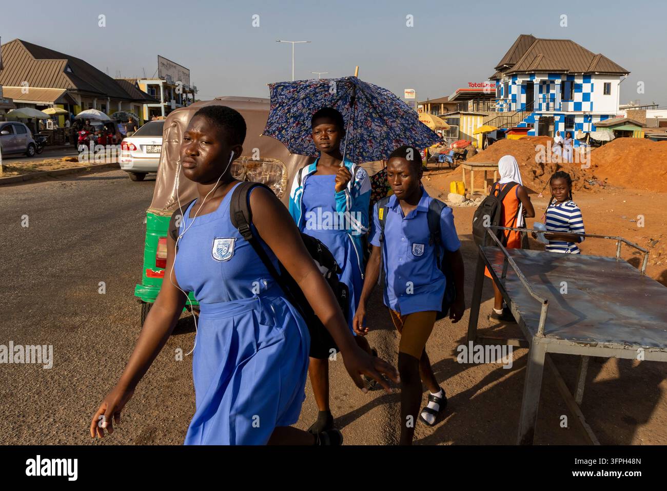 Écoliers en uniformes bleus marchant dans la rue en tenant un parapluie, Région de Bono Est, Kintampo, Ghana Banque D'Images