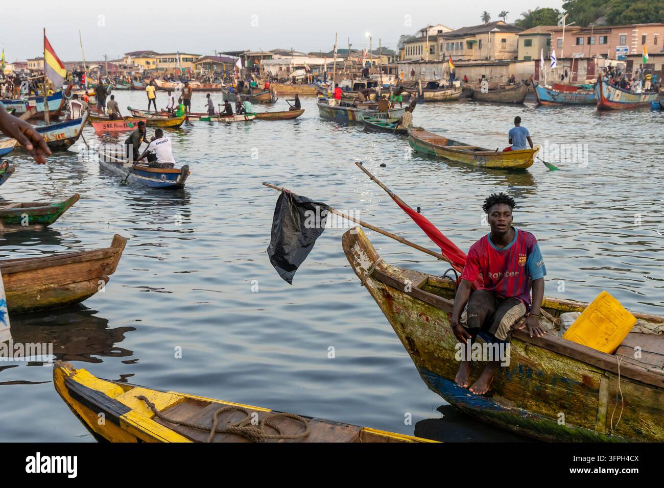 Un jeune homme est assis à la proue d'un bateau de pêche en bois dans le port, région centrale, Elmina, Ghana Banque D'Images
