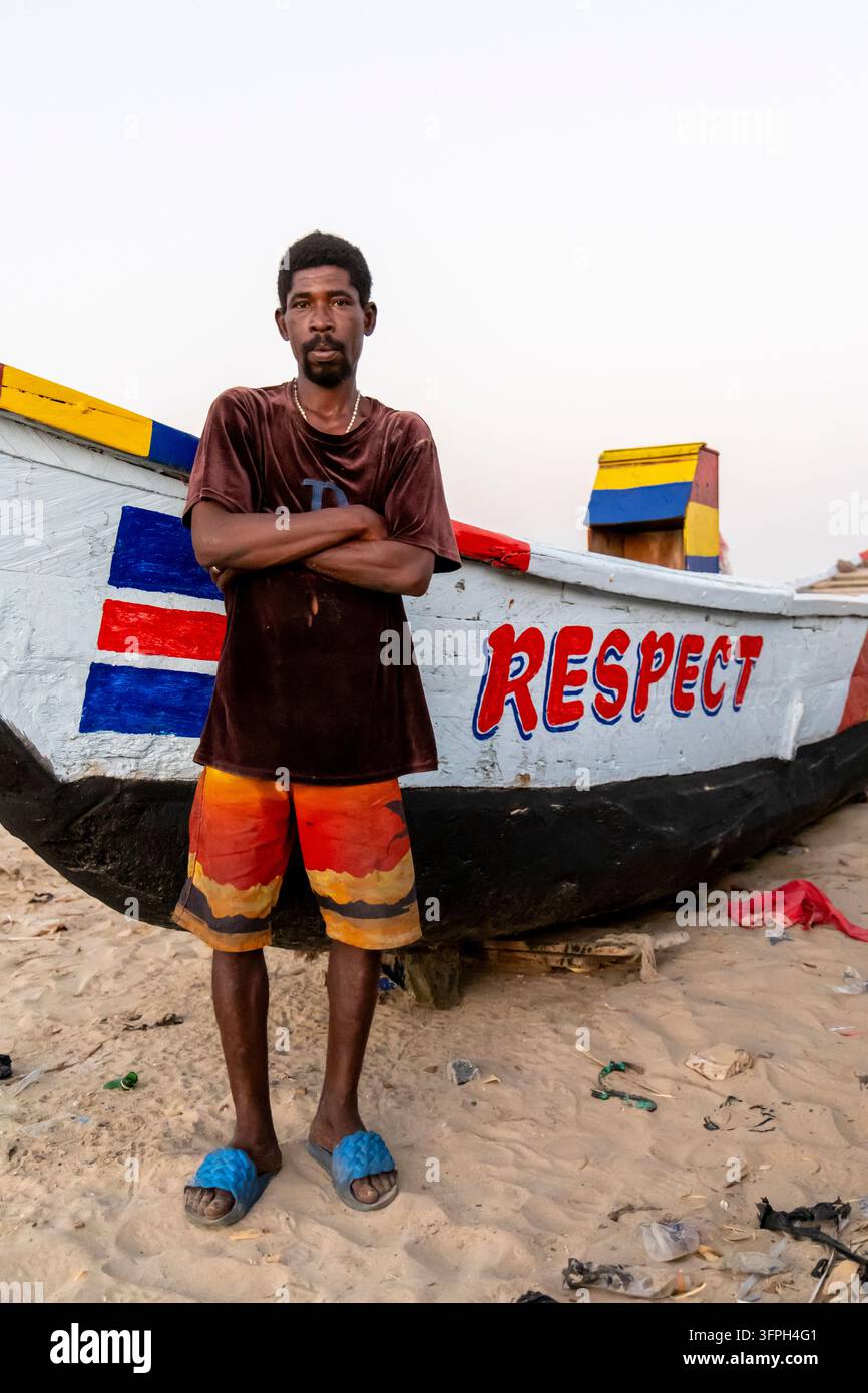 Un pêcheur se tient les bras croisés à côté de son bateau en bois sur la plage, région centrale, Elmina, Ghana Banque D'Images