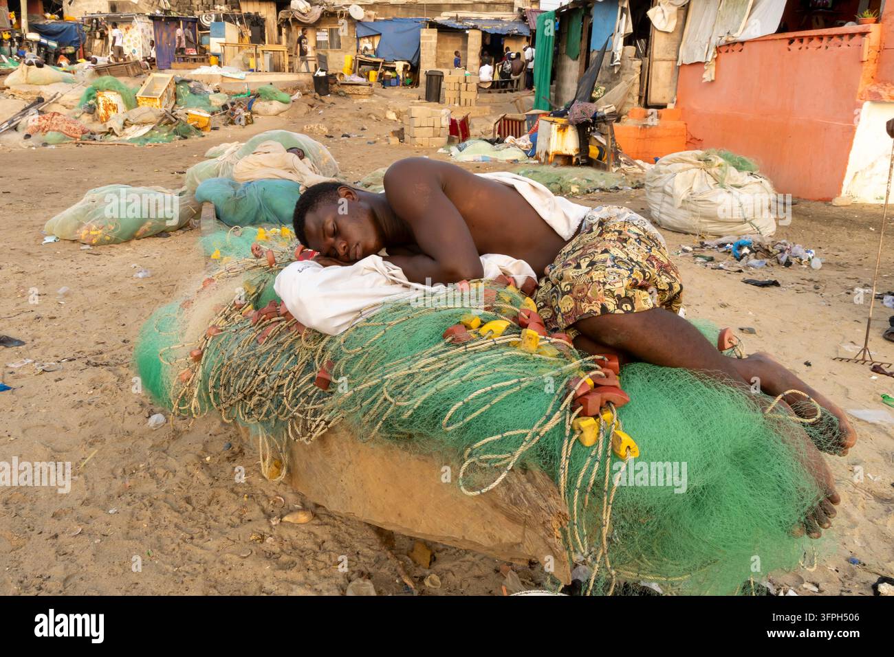 Pêcheur se reposant sur un tas de filets de pêche dans une colonie côtière, région centrale, Cape Coast, Ghana Banque D'Images