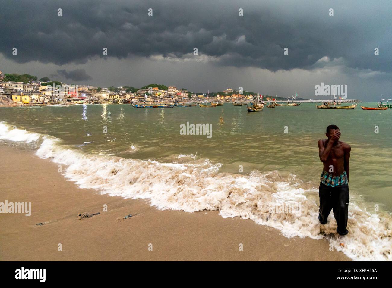 Homme en maillot rayé debout à la proue d'un bateau de pêche en bois avant une tempête, Région centrale, Cape Coast, Ghana Banque D'Images