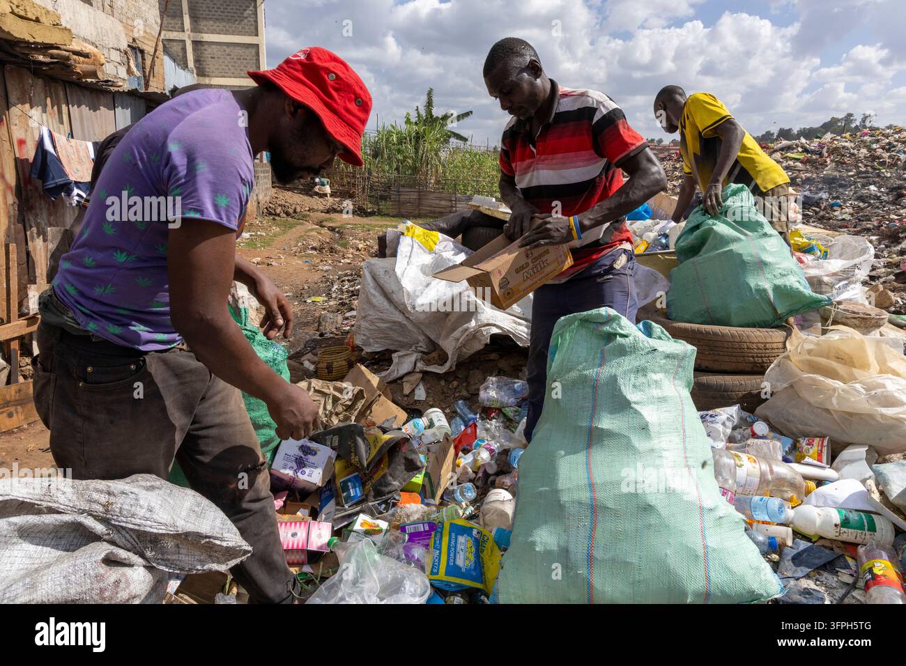 Trois hommes triant des bouteilles en plastique et du carton d'un tas d'ordures dans de grands sacs à côté d'une décharge dans la zone de Kibera, Nairobi County, Nai Banque D'Images