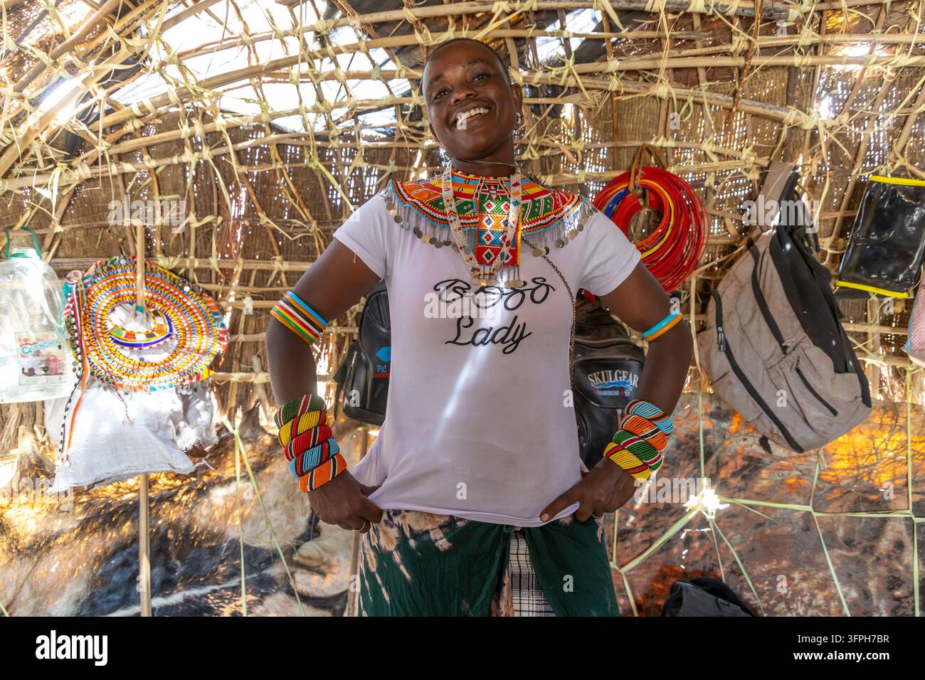 Femme Rendille souriante portant un t-shirt Boss Lady et un collier de perles coloré ainsi que des bracelets dans une hutte tissée traditionnelle au lac Turkana Banque D'Images