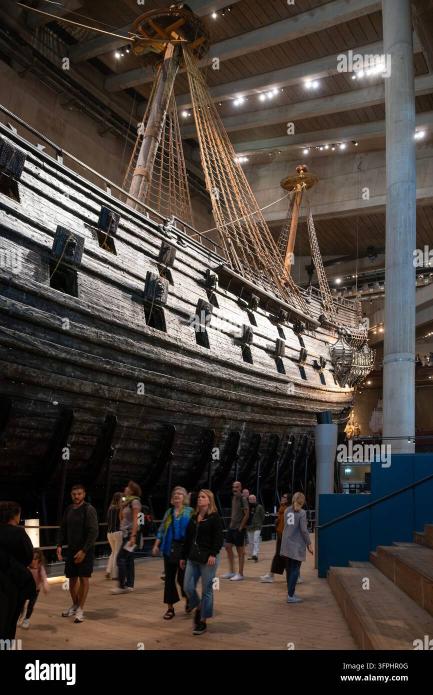 Stockholm, Suède ; 12 août 2026 : des visiteurs du musée marchent à côté de la coque massive en bois sombre et des sabords du navire de guerre Vasa du XVIIe siècle à l'intérieur Banque D'Images