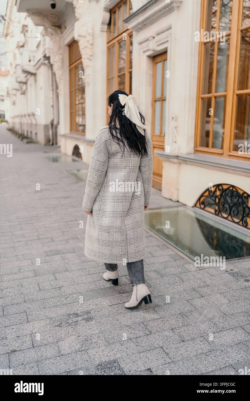 Femme en manteau marchant le long d'un trottoir pavé devant des bâtiments historiques élégants d'Europe lors d'une promenade matinale paisible Banque D'Images