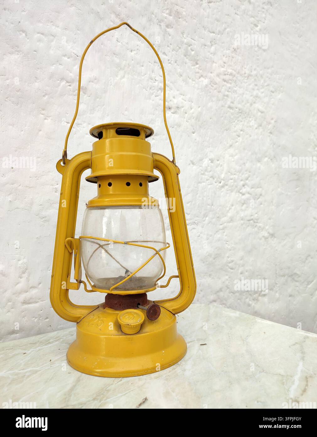 Lanterne à kérosène jaune vintage avec chapeau de verre contre un mur blanc - Image de stock capturée avec un smartphone