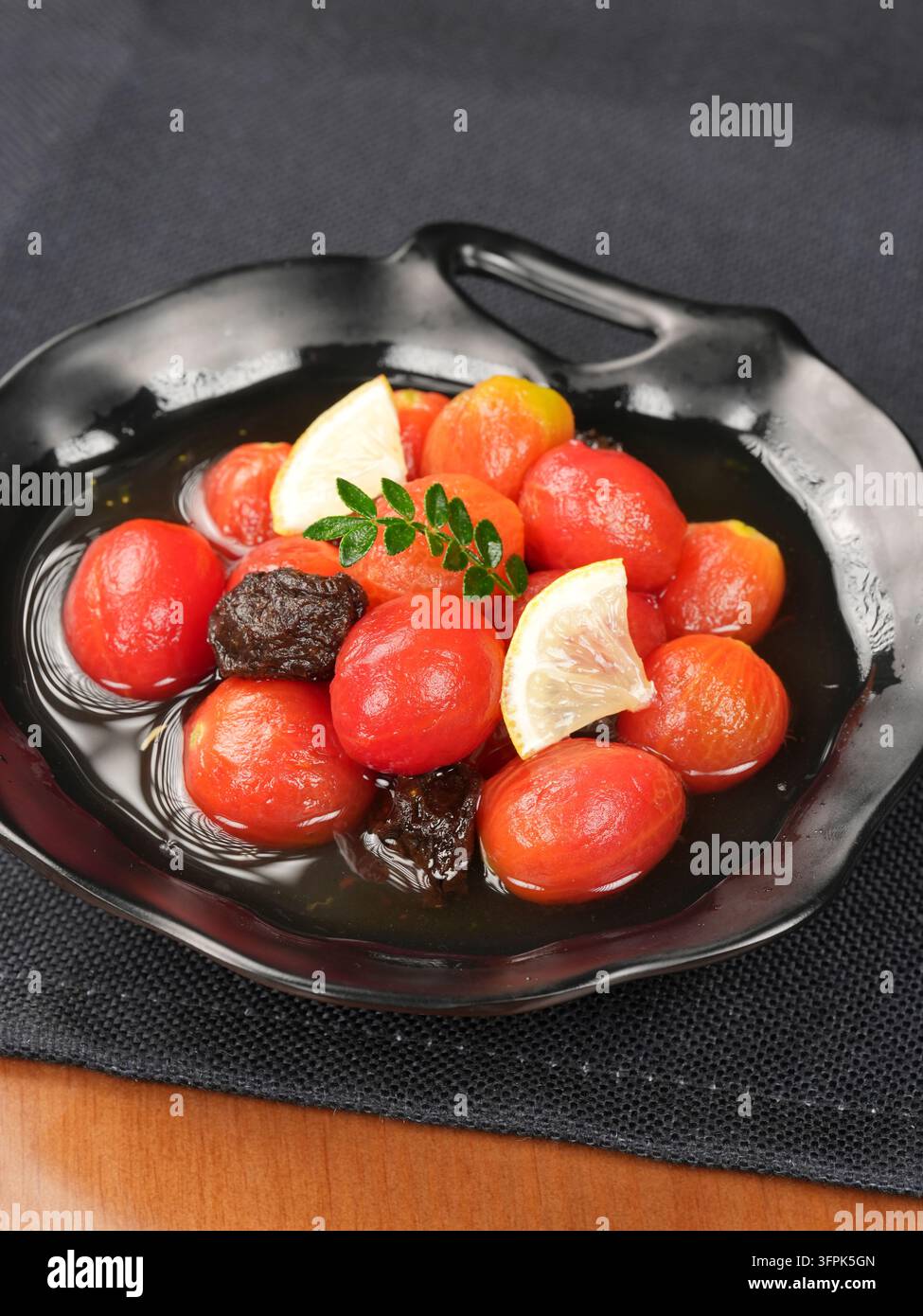 Tomates cerises marinées à la prune conservée sur une assiette en céramique noire, entrée de restaurant Banque D'Images