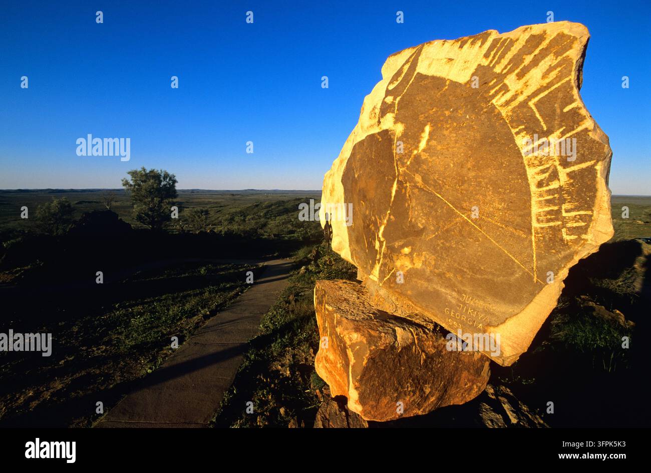 Œuvre d'art en pierre signé Jumber Jikiya, Géorgie 1993, éclairé par le soleil bas à côté d'un sentier surplombant des plaines broussailleuses plates sous un ciel bleu clair. Banque D'Images