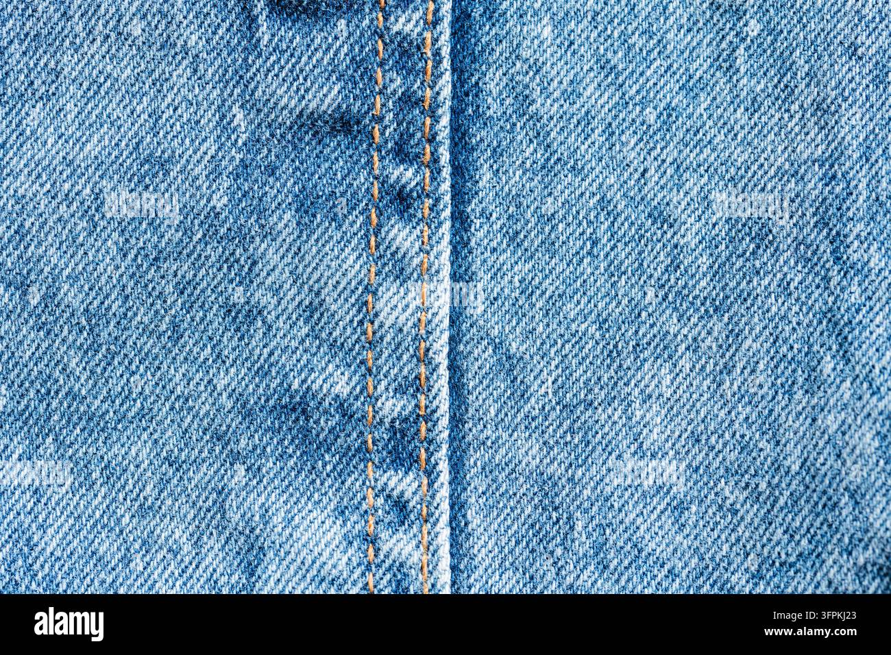 Couture en denim bleu avec des points dorés parallèles et un bord rehaussé sur un fond en tissu sergé diagonal Banque D'Images