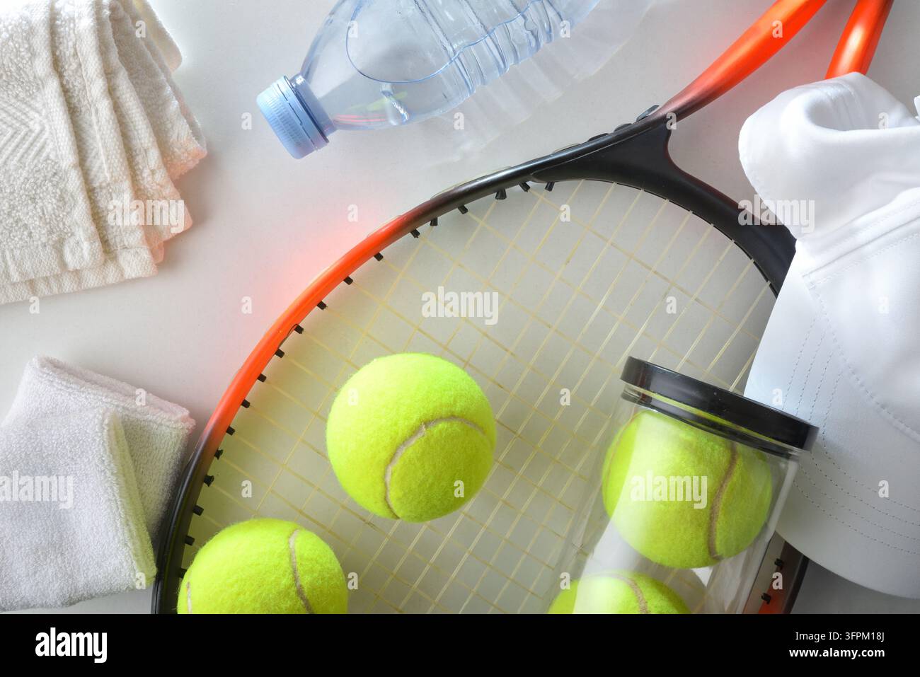 Racket de tennis, balles, bouteille d'eau, serviettes et vêtements de sport disposés sur une surface lumineuse, évoquant la préparation, l'hydratation et une activité athlétique active Banque D'Images