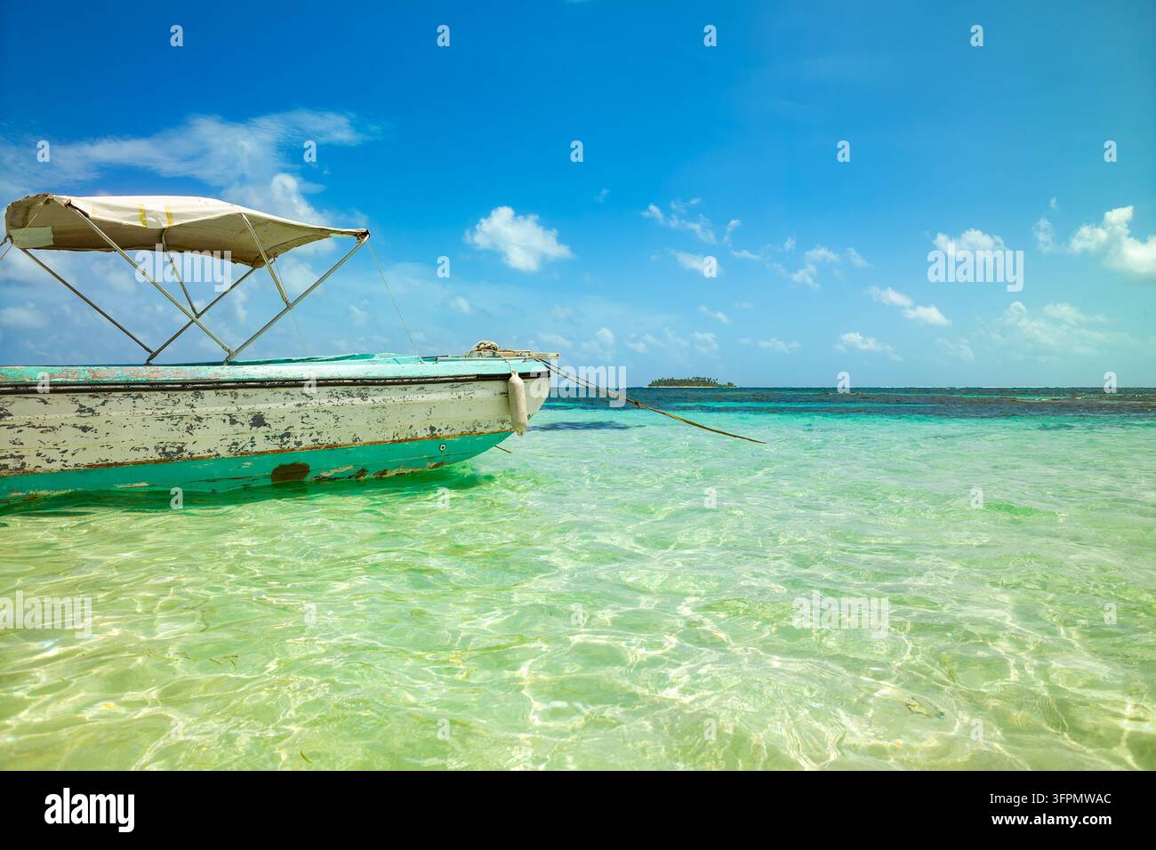 Un bateau usé avec une toile d'ombrage flotte sur une eau turquoise au large de l'île de San Andres, Colombie, avec Johnny Cay couvert de palmiers à l'horizon. Banque D'Images