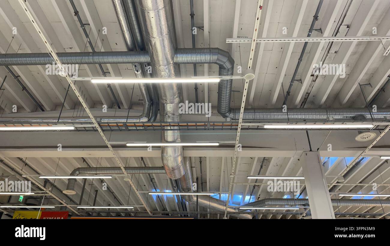 Plafond industriel exposé avec conduits de ventilation métalliques, tuyaux de climatisation et éclairage LED dans un bâtiment commercial Banque D'Images