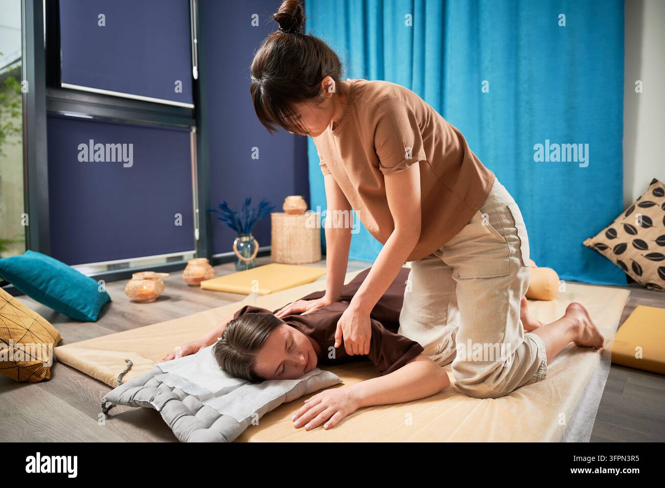 Masseuse faisant massage yoga thaïlandais. Thérapeute de femme faisant le traitement de massage traditionnel pour la patiente féminine à l'intérieur. Client allongé sur tapis, méditant, profitant d'un massage des mains dans une atmosphère calme. Banque D'Images