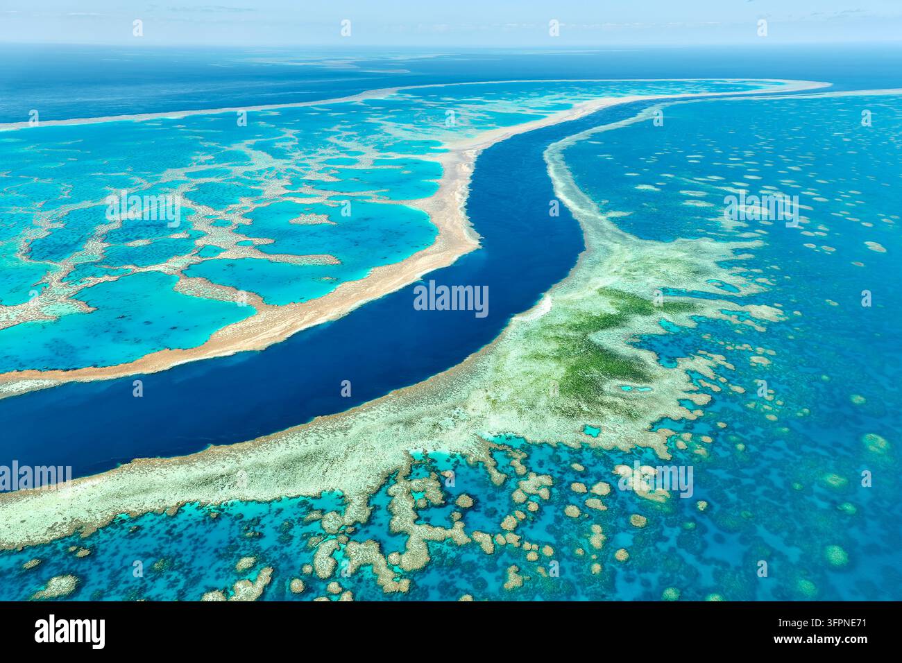 Vue aérienne d'un canal bleu profond serpentant entre des plats de récif peu profonds et des lagons turquoise dans la mer de Corail au large du Queensland Banque D'Images