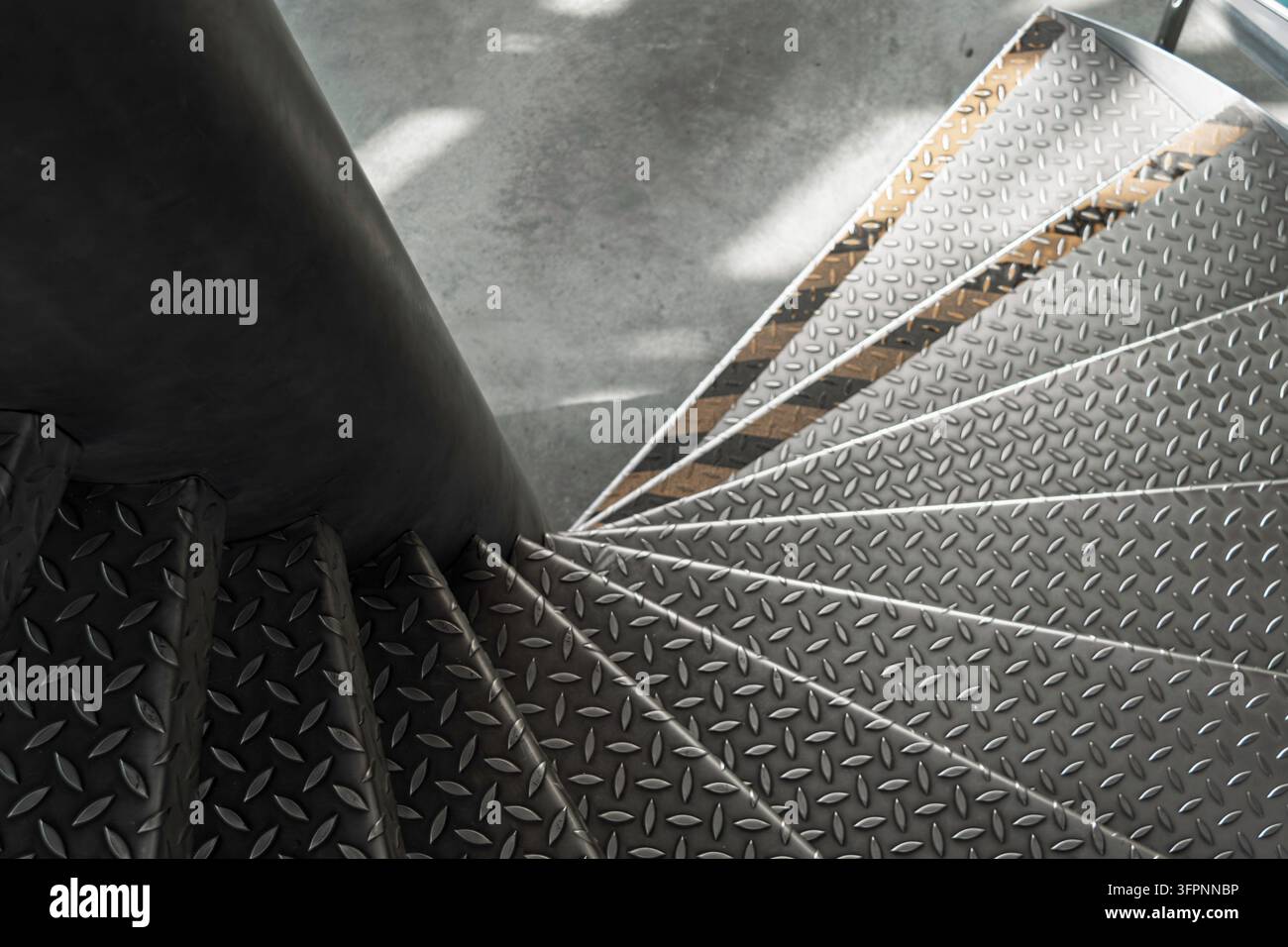 Vue aérienne d'un escalier en colimaçon métallique industriel dans un atrium, de fortes lignes radiales et des taches de lumière douce façonnent une composition austère. Banque D'Images
