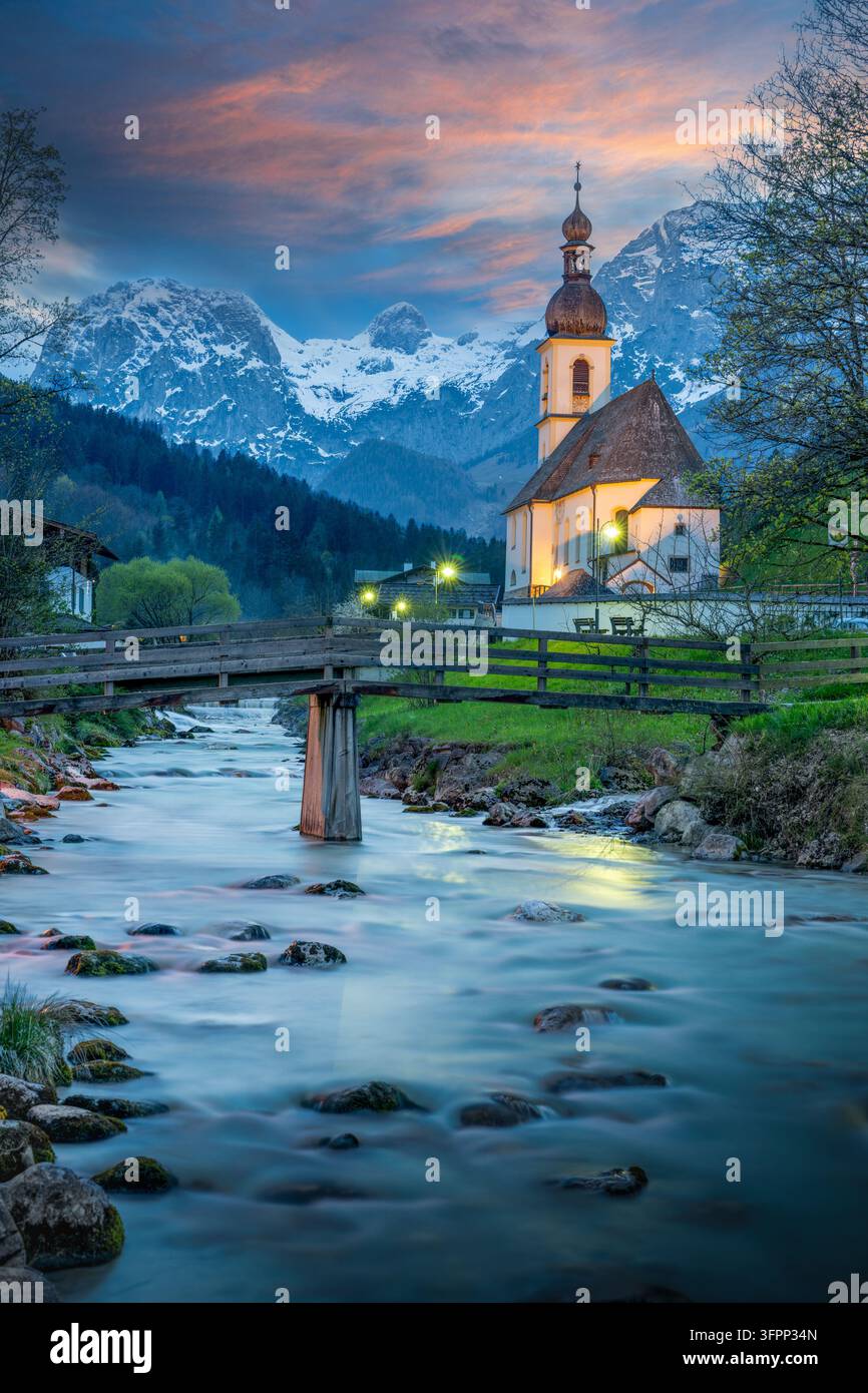 Photographie à longue exposition du coucher de soleil de l'église paroissiale Saint-Sébastien à Ramsau bei Berchtesgaden, Allemagne. Une rivière alpine douce coule devant le bois Banque D'Images