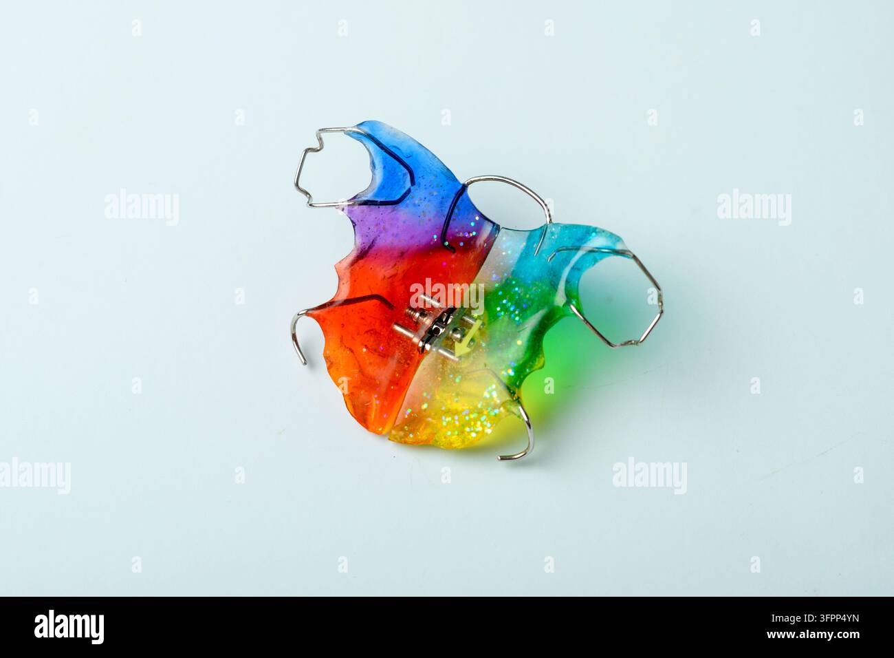 L'aligner orthodontique à paillettes arc-en-ciel repose sur un fond blanc pour l'alignement dentaire pédiatrique et le traitement par appareil amovible. Banque D'Images
