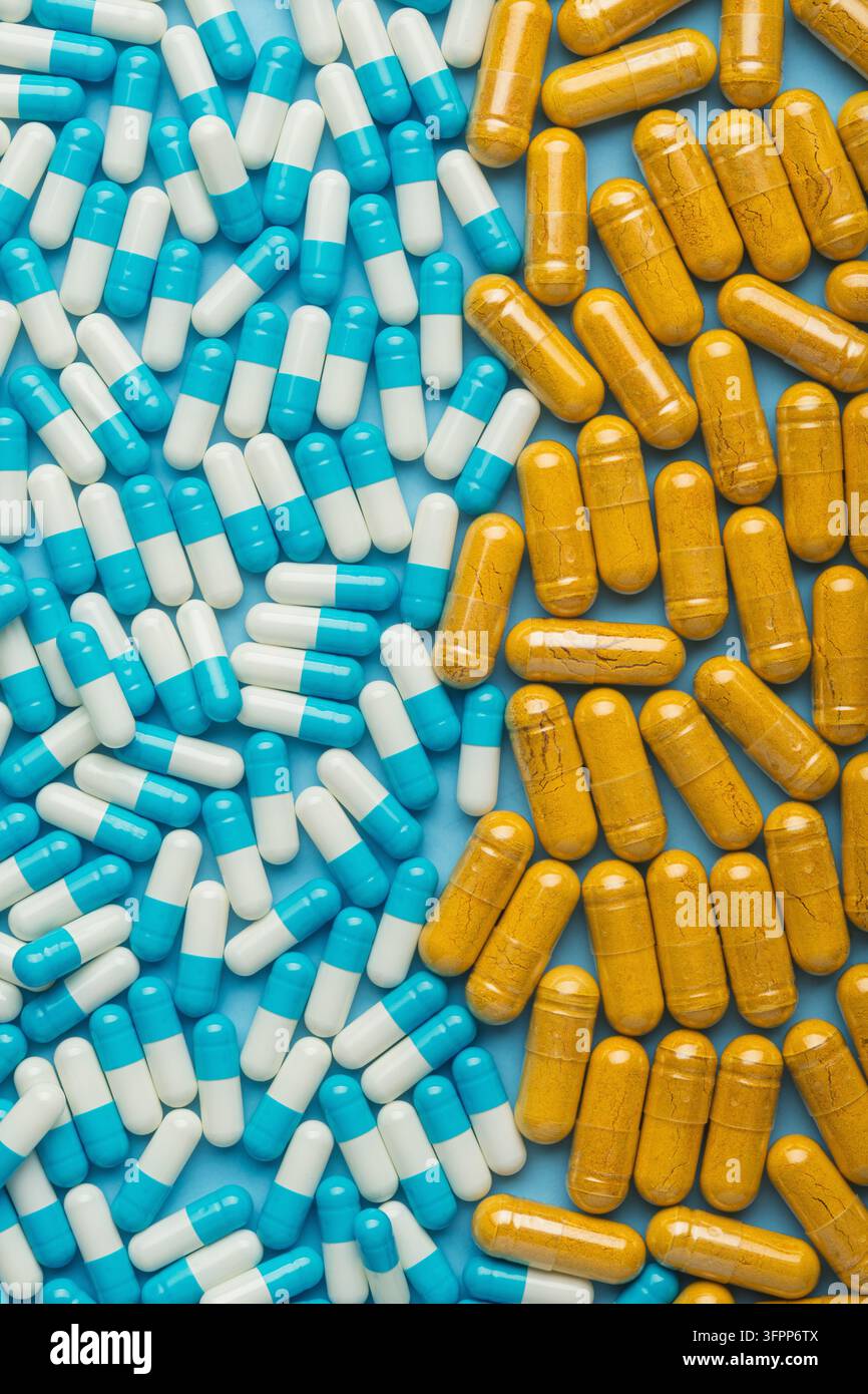 Gélules bleues et blanches face à des pilules jaunes de compléments herbaires sur un fond turquoise, concept de choix et de comparaison des médicaments. Banque D'Images