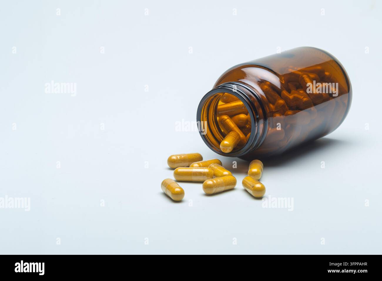 Une bouteille de supplément ambré posée sur le côté avec des capsules jaunes sur un fond clair, espace de copie calme et propre pour la promotion du produit. Banque D'Images