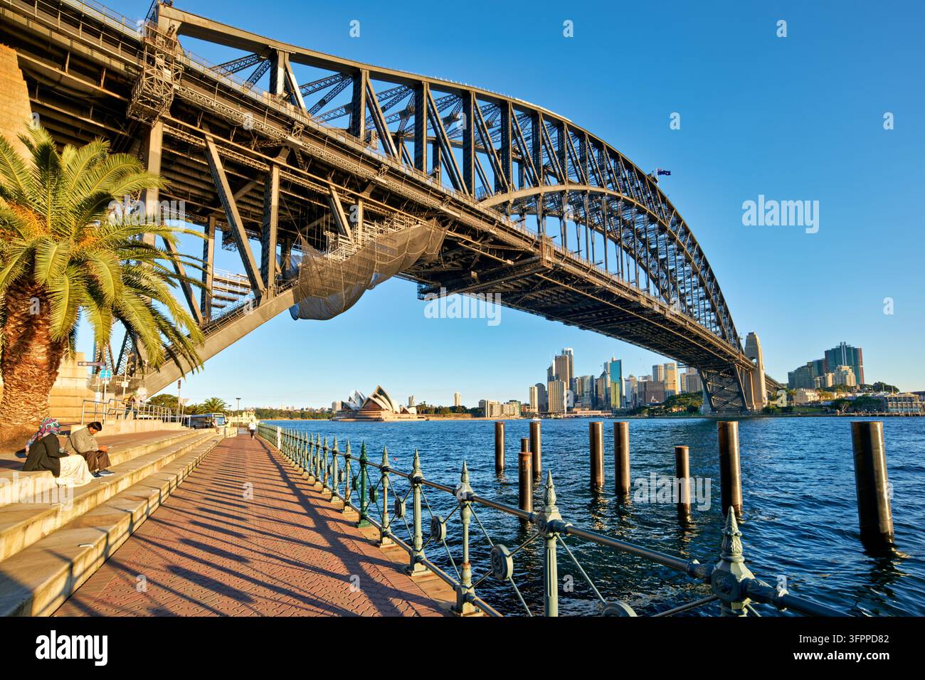 Promenade riveraine sous la travée en arc d'acier, avec la ligne d'horizon du centre-ville de Sydney à travers Port Jackson sous le soleil du tardif après-midi, Nouvelle-Galles du Sud Banque D'Images