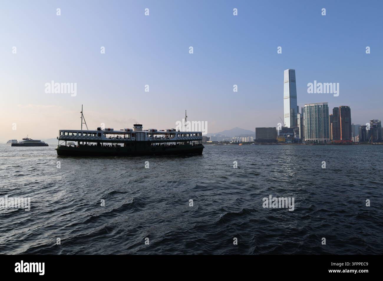 HONG KONG - 23 SEPTEMBRE 2026 : Un bateau traditionnel Star Ferry naviguant sur le Victoria Harbour avec la skyline de West Kowloon et le bâtiment ICC en arrière-plan Banque D'Images