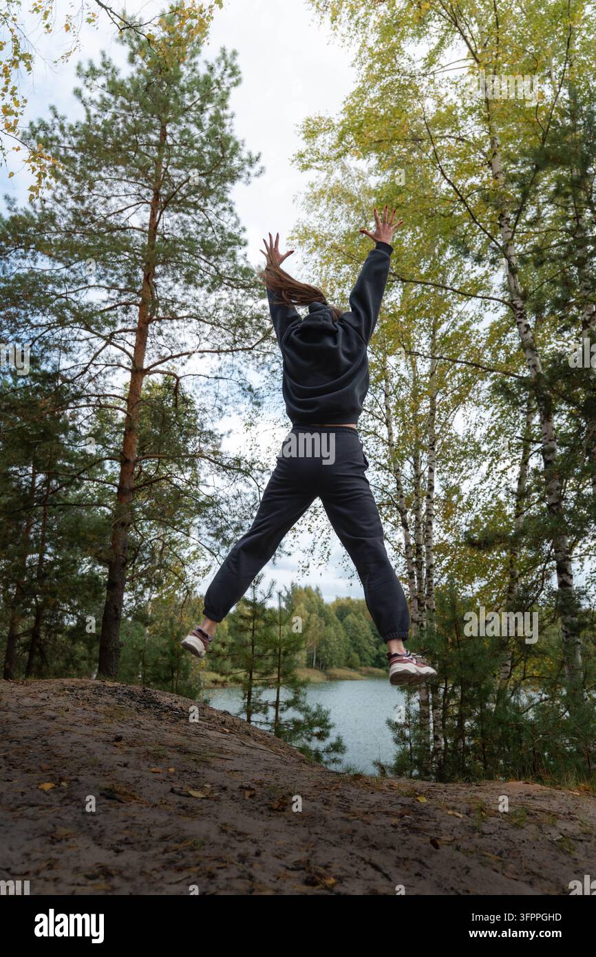 Femme joyeuse sautant haut au-dessus d'un sentier forestier lors d'un voyage de retraite bien-être paisible en forêt Banque D'Images