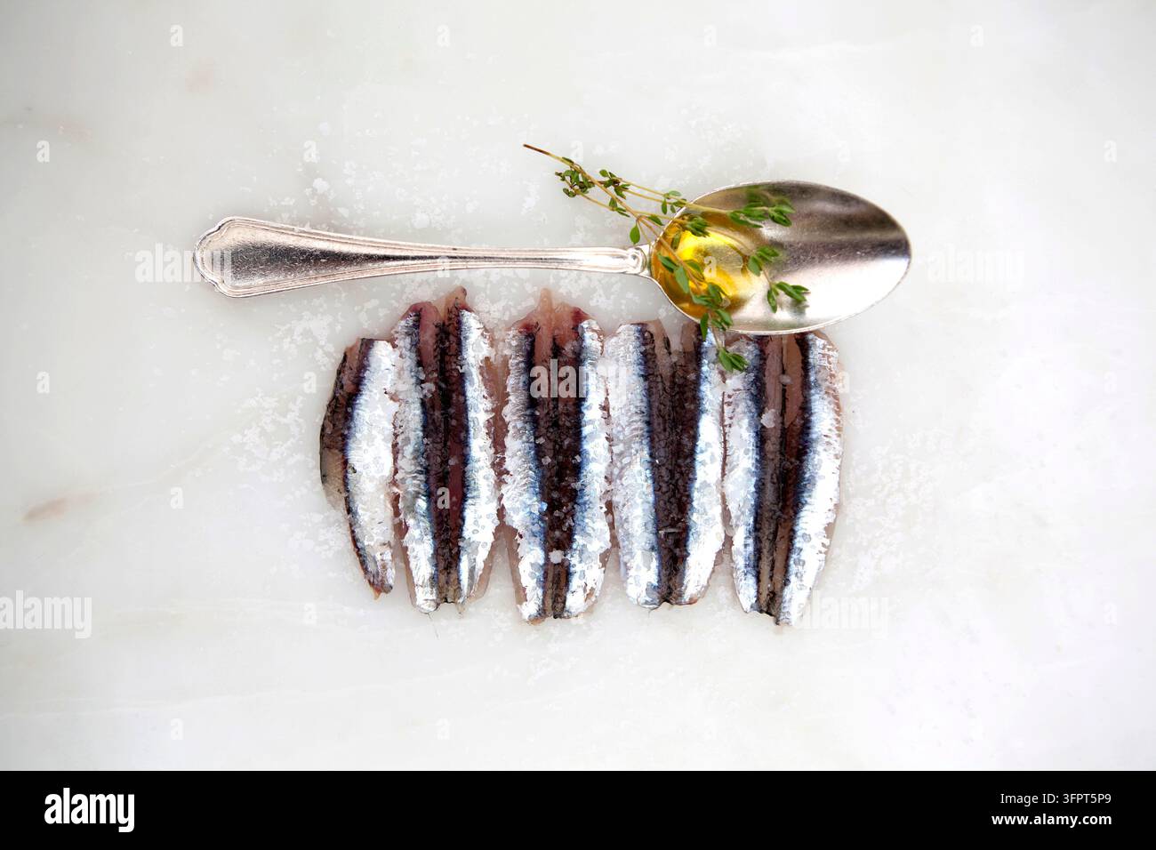 Poisson salé avec une cuillère en argent et des herbes sur une surface blanche Banque D'Images