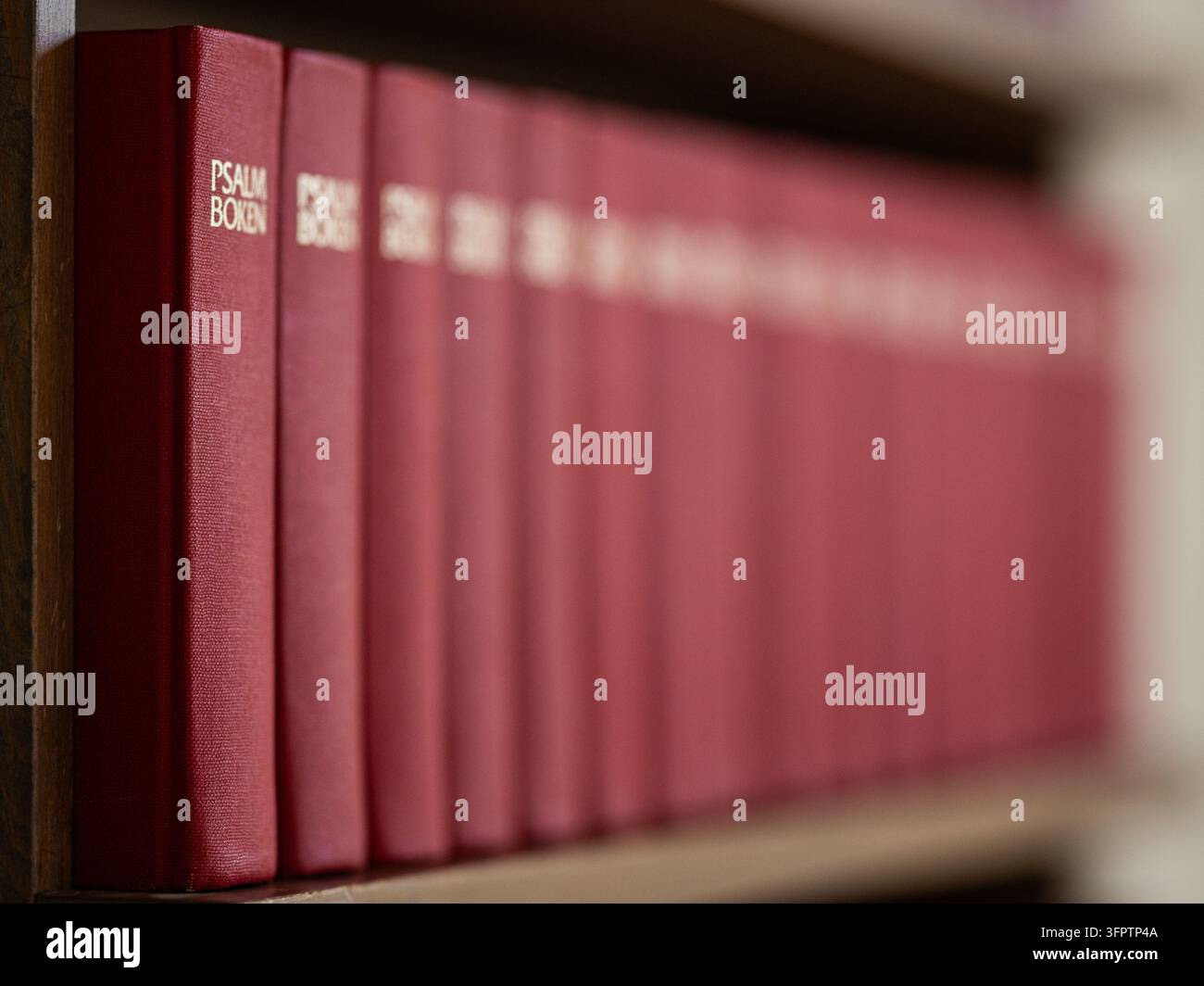 Rangeée de livres d'hymnes suédois rouges sur une étagère en bois à l'intérieur de l'église de Puottaure dans le nord de la Suède, photographiée avec une profondeur de champ peu profonde. Banque D'Images