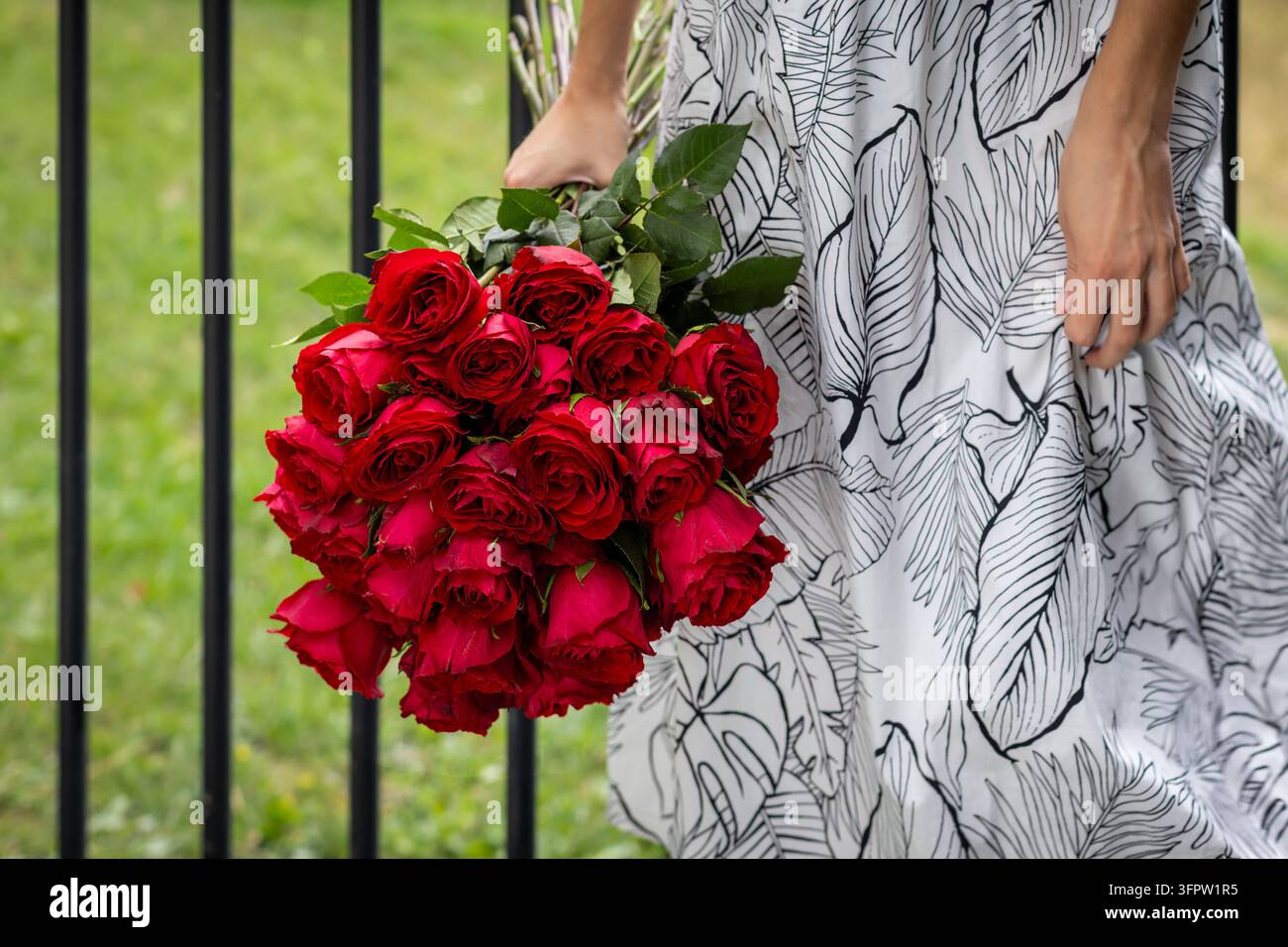 Femme en robe blanche fleurie élégante tenant un bouquet luxuriant de roses rouges éclatantes en plein air, gros plan de fleurs romantiques symbolisant l'amour et la passion sur Banque D'Images