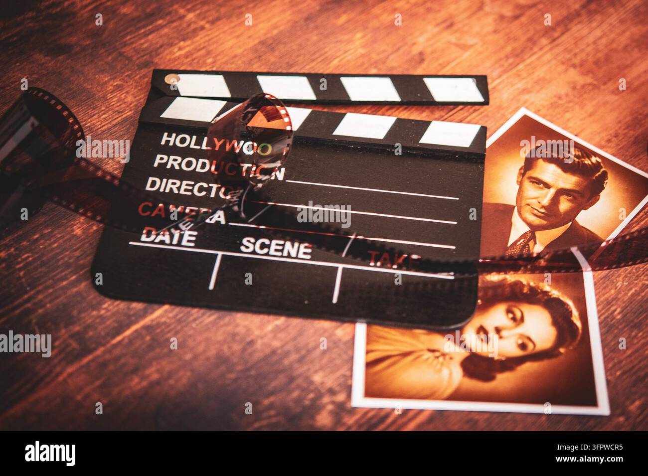 nature morte cinématographique sépia avec une claquette de film hollywoodien, une bande de film enroulée et deux photographies de portrait de style vintage sur bois Banque D'Images