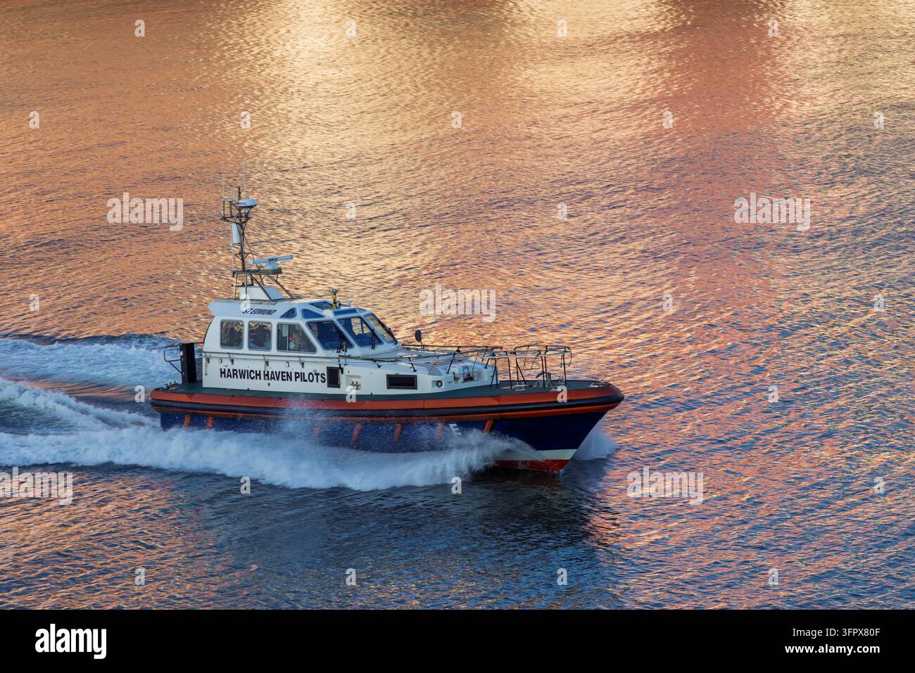 Harwich, Angleterre, 25 août 2026 : Un bateau-pilote file le long de la rivière à côté d'un quai industriel à Harwich, Royaume-Uni, produisant une forte vague blanche Banque D'Images