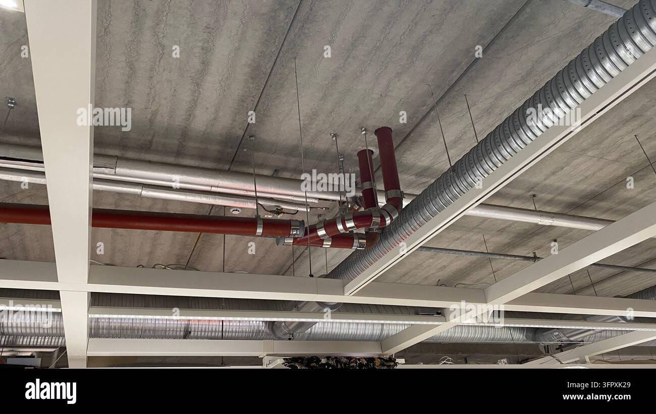 Conduits de ventilation exposés et tuyaux industriels installés sous un plafond en béton dans un bâtiment commercial moderne Banque D'Images