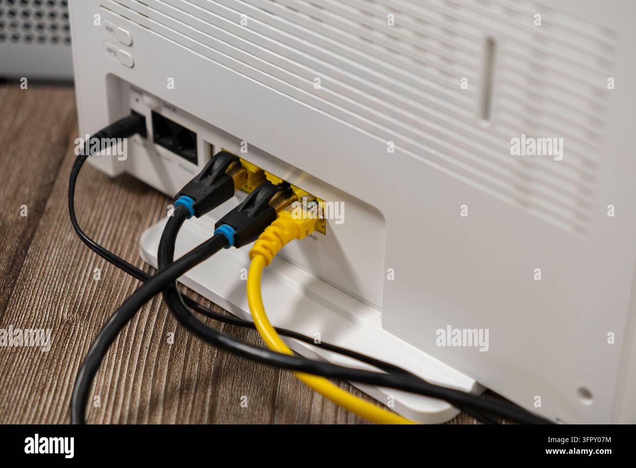 Grossissement d'un routeur Internet avec des câbles jaunes et noirs branchés aux ports sur un bureau en bois, illustrant une connexion haut débit fiable pour l'informatique Banque D'Images