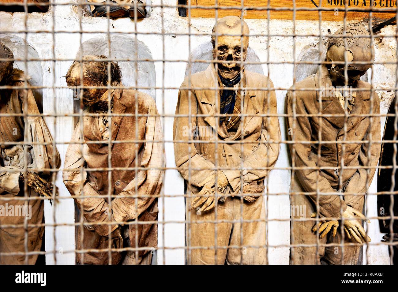 Des corps momifiés en costumes pour hommes se dressent dans des niches murales derrière des grilles métalliques aux Catacombes dei Cappuccini, Palermo, Sicile, Italie Banque D'Images