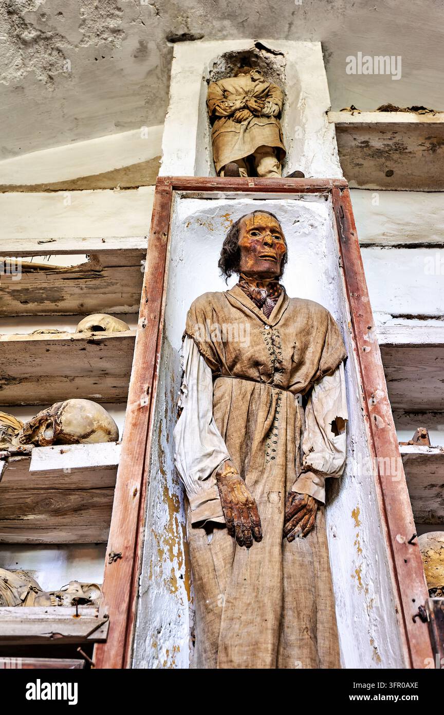 Momie habillée debout dans une niche murale encadrée de bois parmi des crânes sur des étagères à l'intérieur des catacombes capucines de Palerme, Italie Banque D'Images