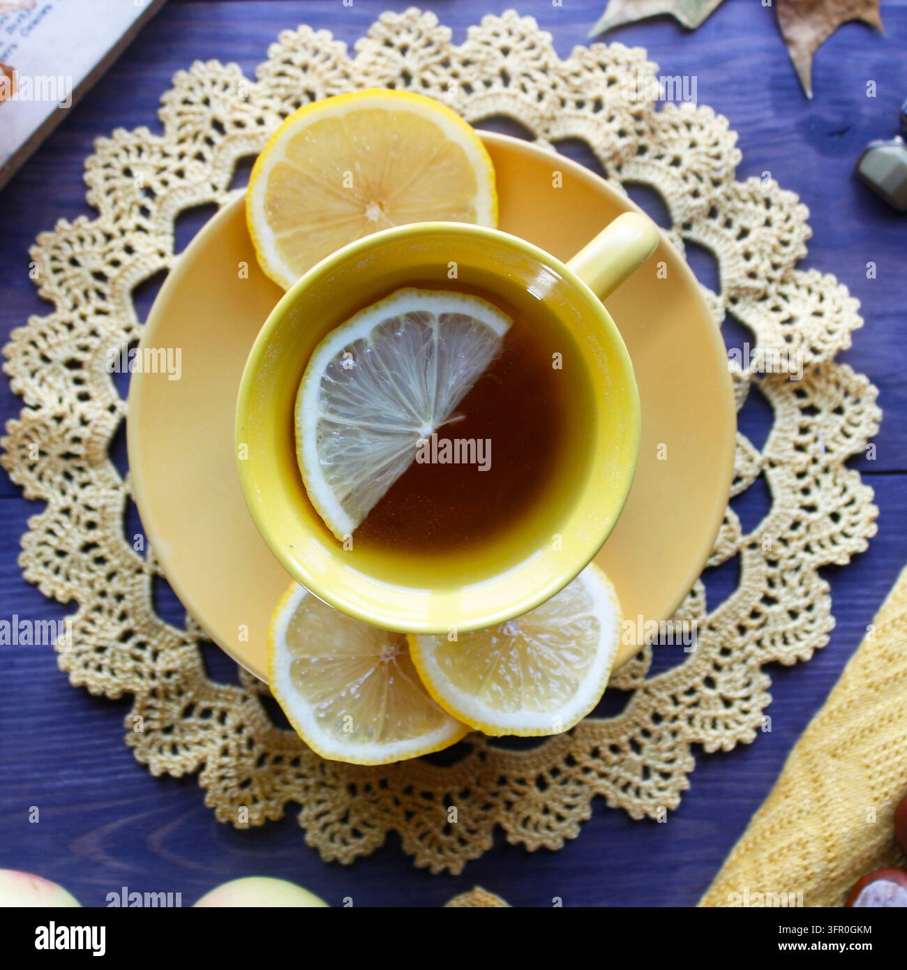 Composition automnale douillette avec une tasse de thé jaune au citron, une napperon en dentelle au crochet et des feuilles faites à la main, un livre ouvert, des pommes et des châtaignes sur du bois sombre Banque D'Images