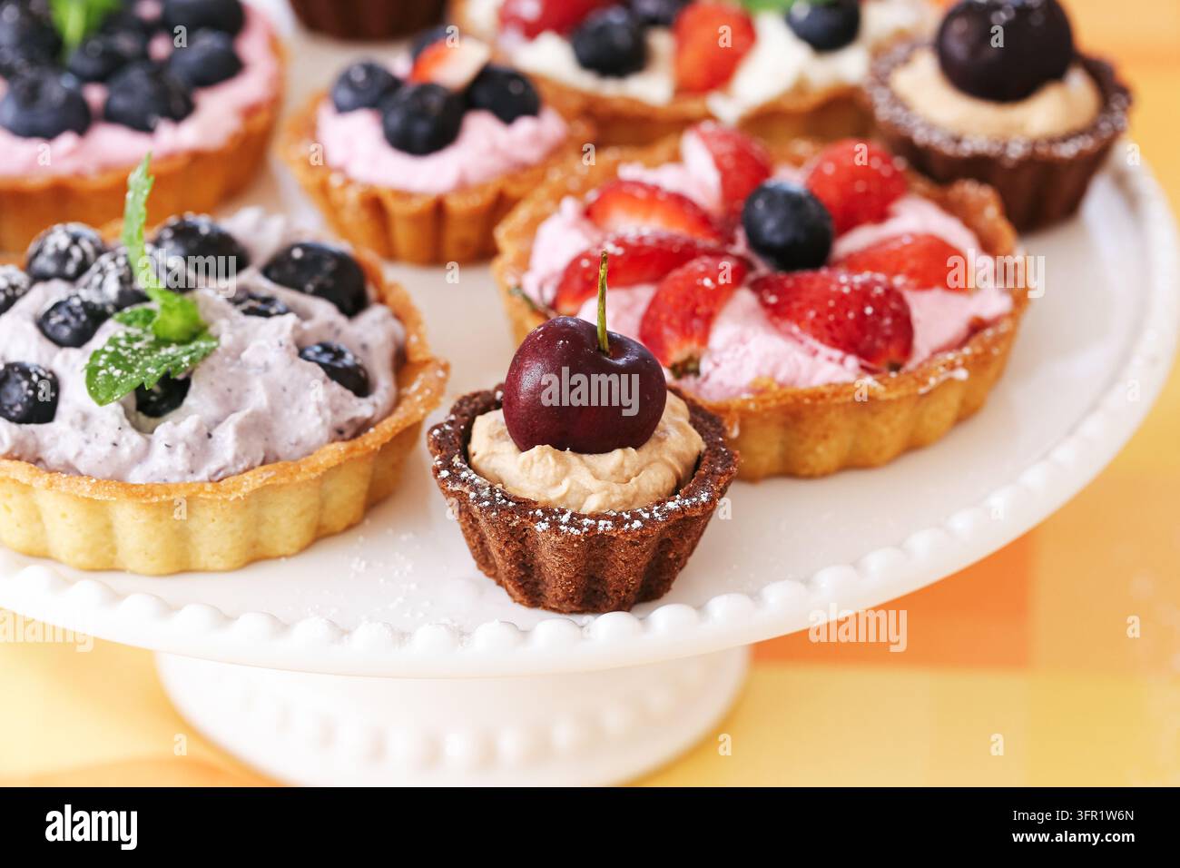 Mini tartes aux fruits assorties avec des baies, des cerises et de la crème sur un présentoir à gâteau blanc. Fond de dessert pour des pâtisseries sucrées, des friandises de fête et des célébrations Banque D'Images
