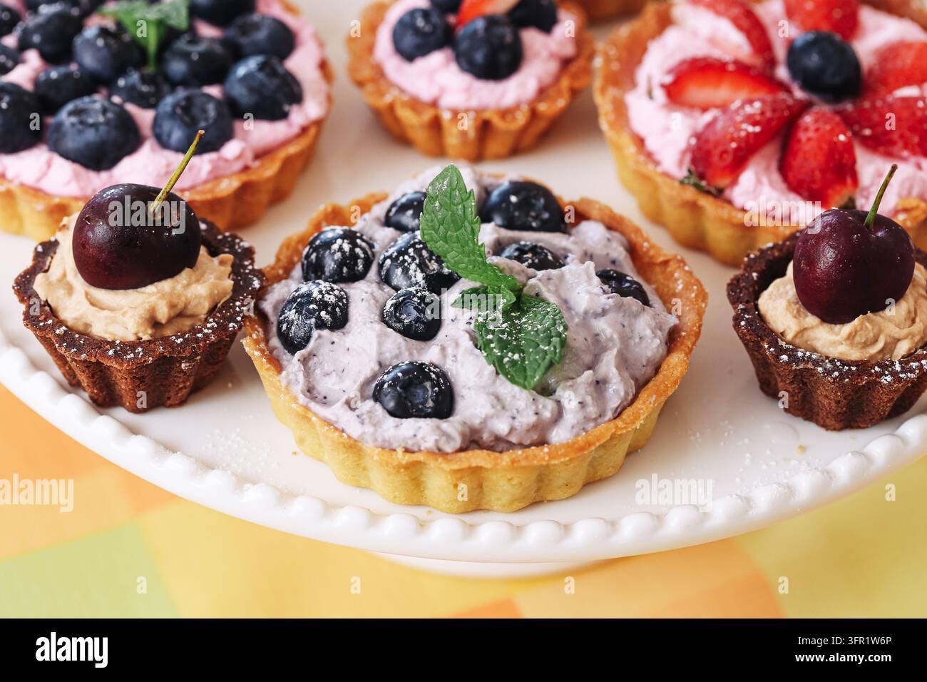 Mini tartes aux fruits assorties avec des baies et de la crème sur un plat de service blanc. Fond de dessert pour les pâtisseries sucrées, la nourriture de fête et les célébrations. Banque D'Images