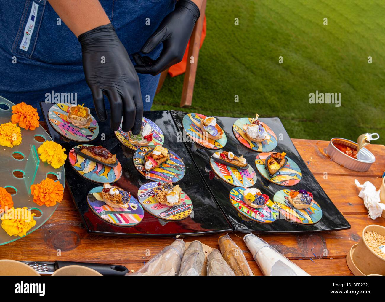 Chef en gants noirs dressant des canapés gastronomiques sur des assiettes décoratives en plein air Banque D'Images